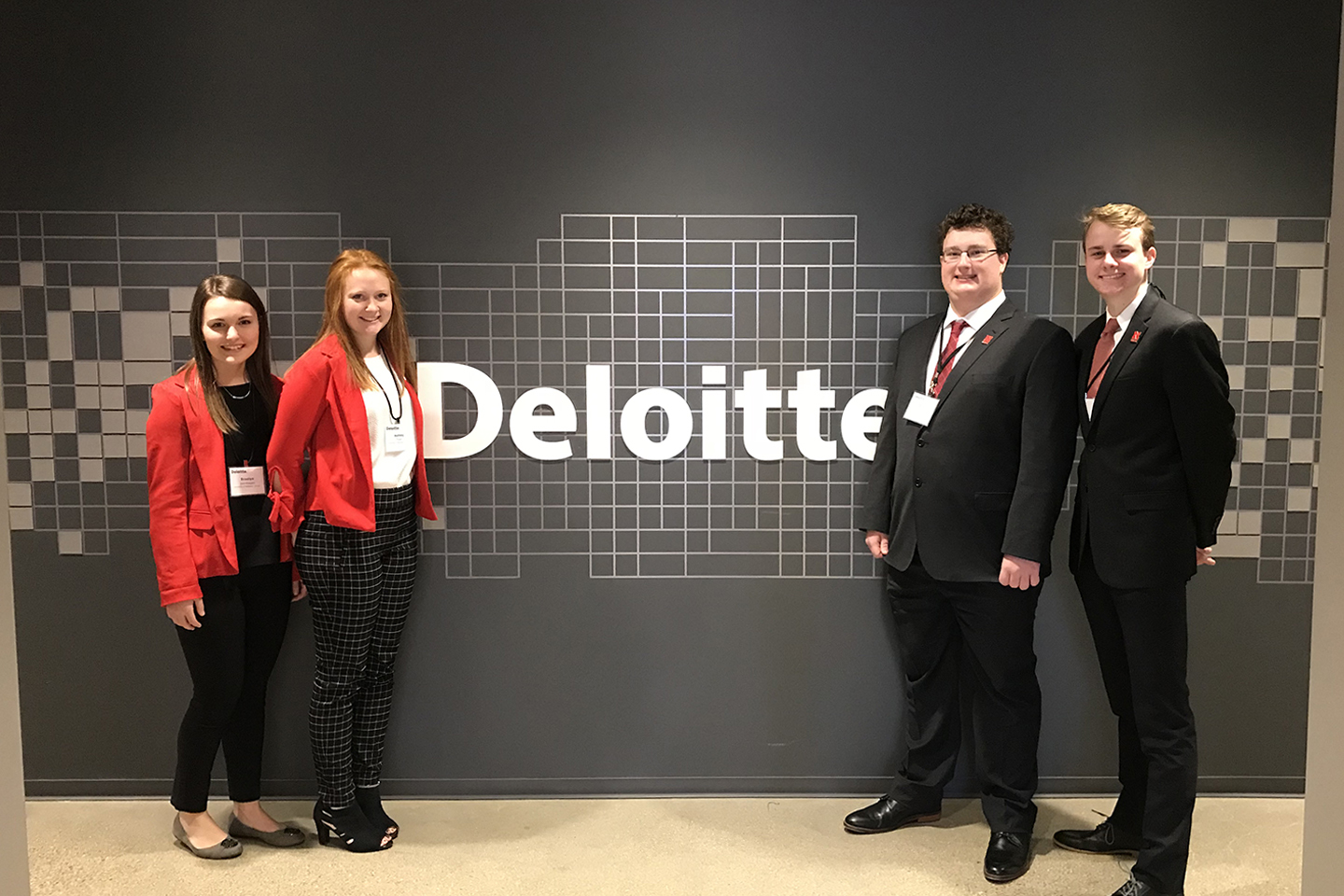 four students standing in front of the deloitte logo