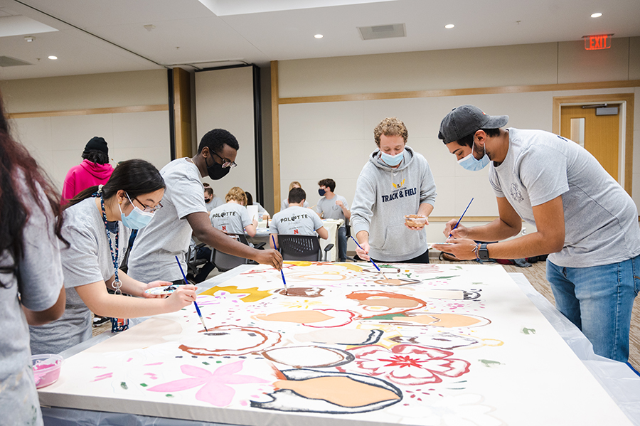 Many students painting on the mural canvas