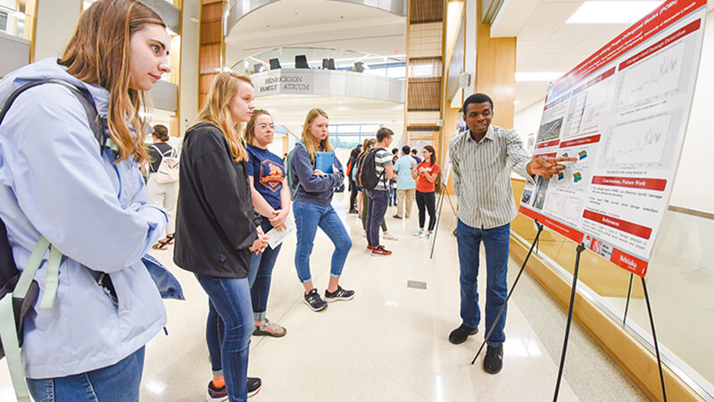 Students listening to another present at research fair