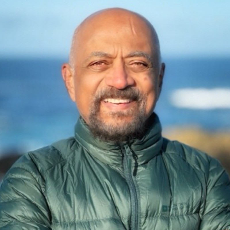 Suresh Subramanian; Man in a green puffer jacket with blurred face, standing outdoors near the ocean.
