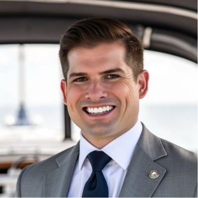 Rick Cantril; Man in a gray suit and blue tie, standing in front of a blurred nautical background.
