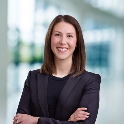 Sarah Cast: Person in business attire standing with arms crossed in a blurred office environment.
