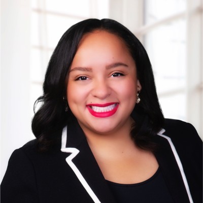 Liz Codina: Professional person with dark hair in a black blazer, blurred for privacy, in a bright office setting.