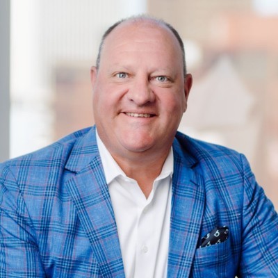 Gary Grote; Man in blue plaid blazer and white shirt with blurred face, seated indoors.