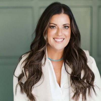 Steph Ledbetter: A woman with long brown hair wearing a white top and turquoise necklace, standing before a green background.