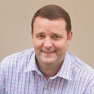 Andy Romjue; Man in a plaid shirt with blurred face against a beige background.