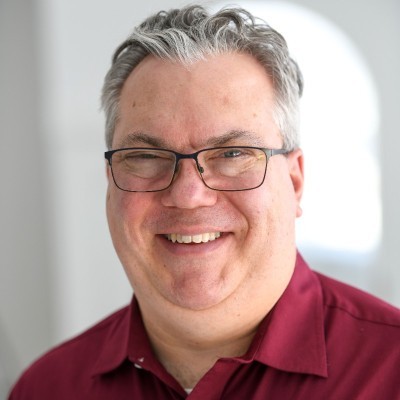 Thad Standley; Man in a red shirt with a blurred face standing indoors.