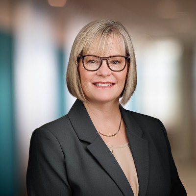 Ellen Dasher; Professional woman in a blazer, standing in a softly lit office hallway.