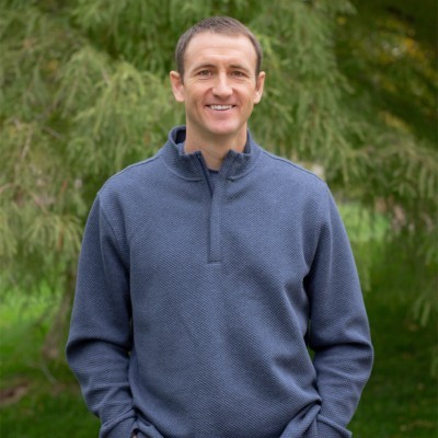 Justin Feerhusen; Man in a blue sweater standing outdoors near trees.