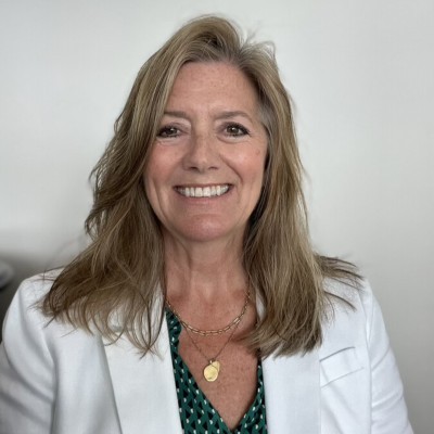 Karmen Hoxie; Woman wearing a white blazer and green patterned shirt with layered gold necklaces.