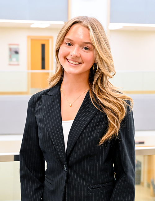 Professional woman in a black pinstripe blazer standing in bright indoor setting.