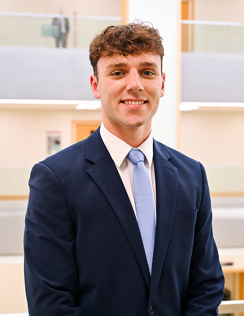 Man in a blue suit and tie standing indoors, blurred face, office background with soft lighting.