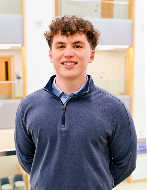 Person wearing a navy quarter-zip sweater in a modern building with glass railings.