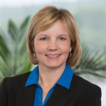 Patricia Thraen; A person in a blue shirt and black blazer indoors with blurred greenery in the background.