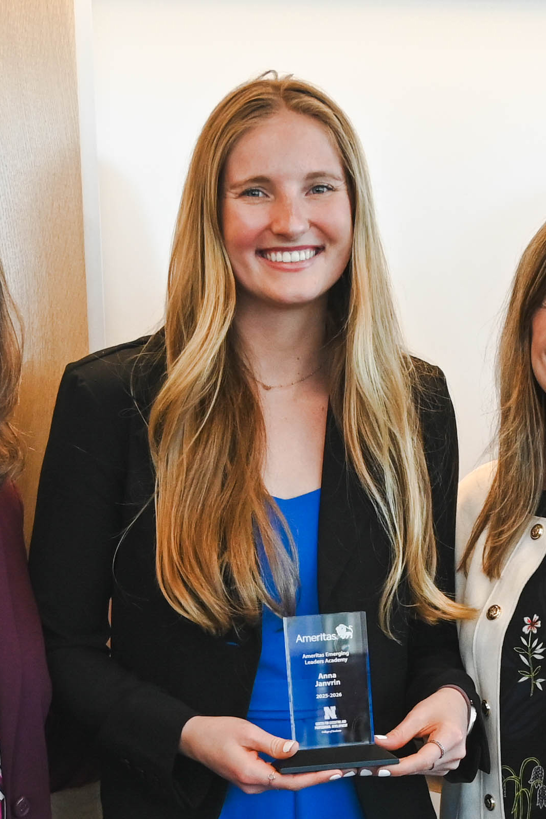 Woman in a black jacket holding a clear award, flanked by two others on a white background.