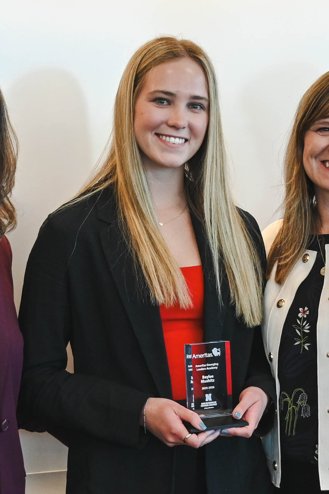 Woman holding a plaque while standing with others; blurred face and formal attire visible.