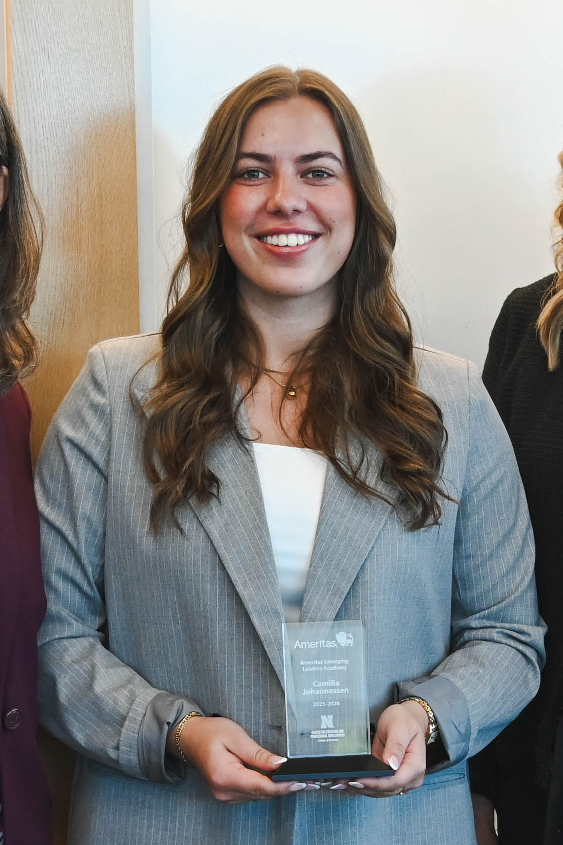 Woman holding a glass award, wearing a gray blazer, standing between two others.