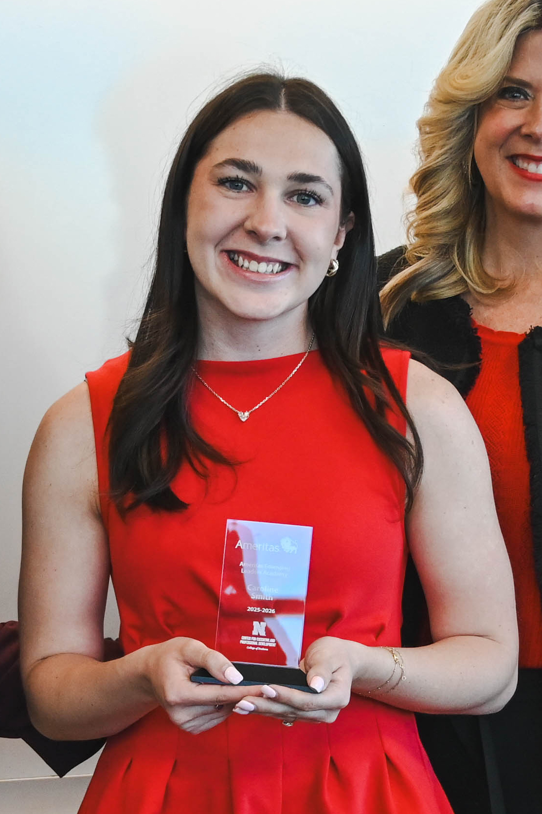 Woman in a red dress holds a glass award, standing next to another smiling woman.