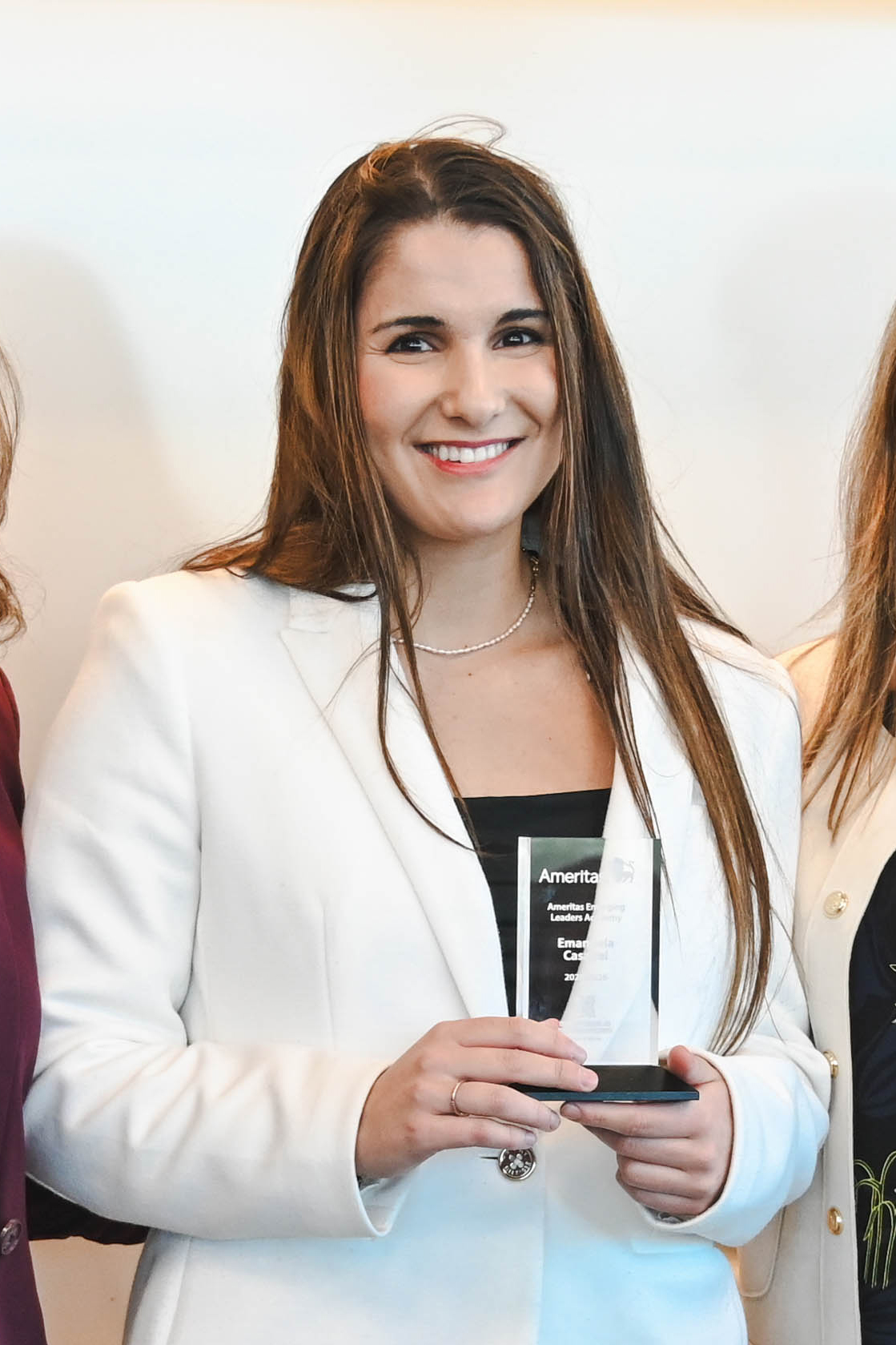 Woman in a white blazer holding a glass award, standing indoors.