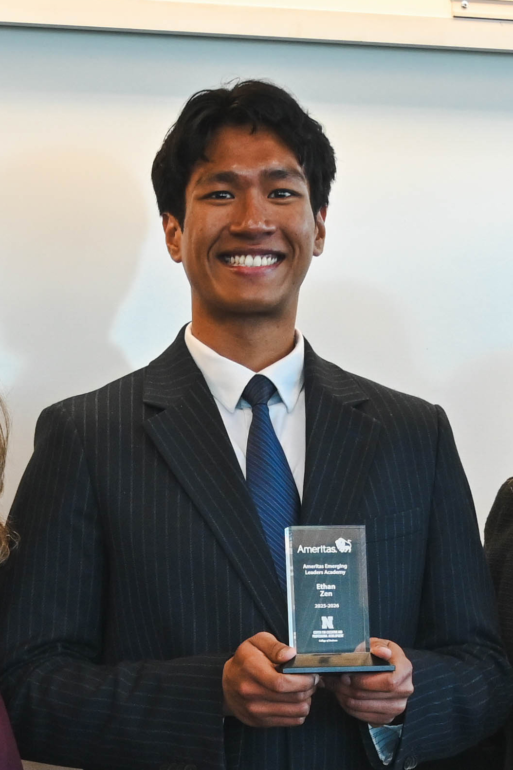 Man in a pinstripe suit holding a glass award in a professional setting.
