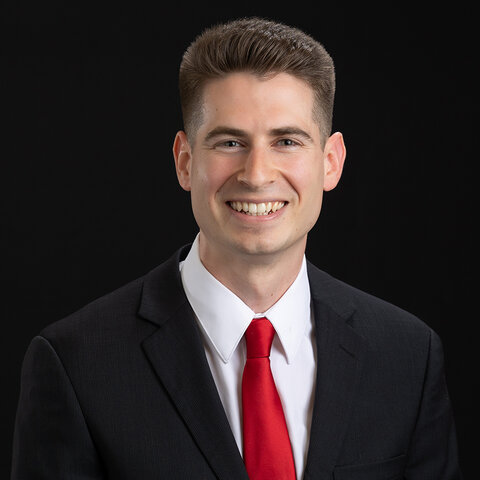 Man in a suit with red tie against a black background.