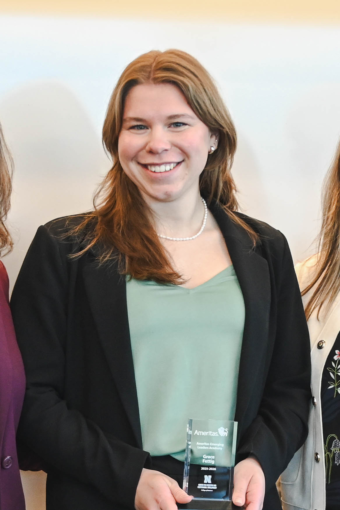 Individual holding an award, wearing a green blouse and black blazer, standing between two others.
