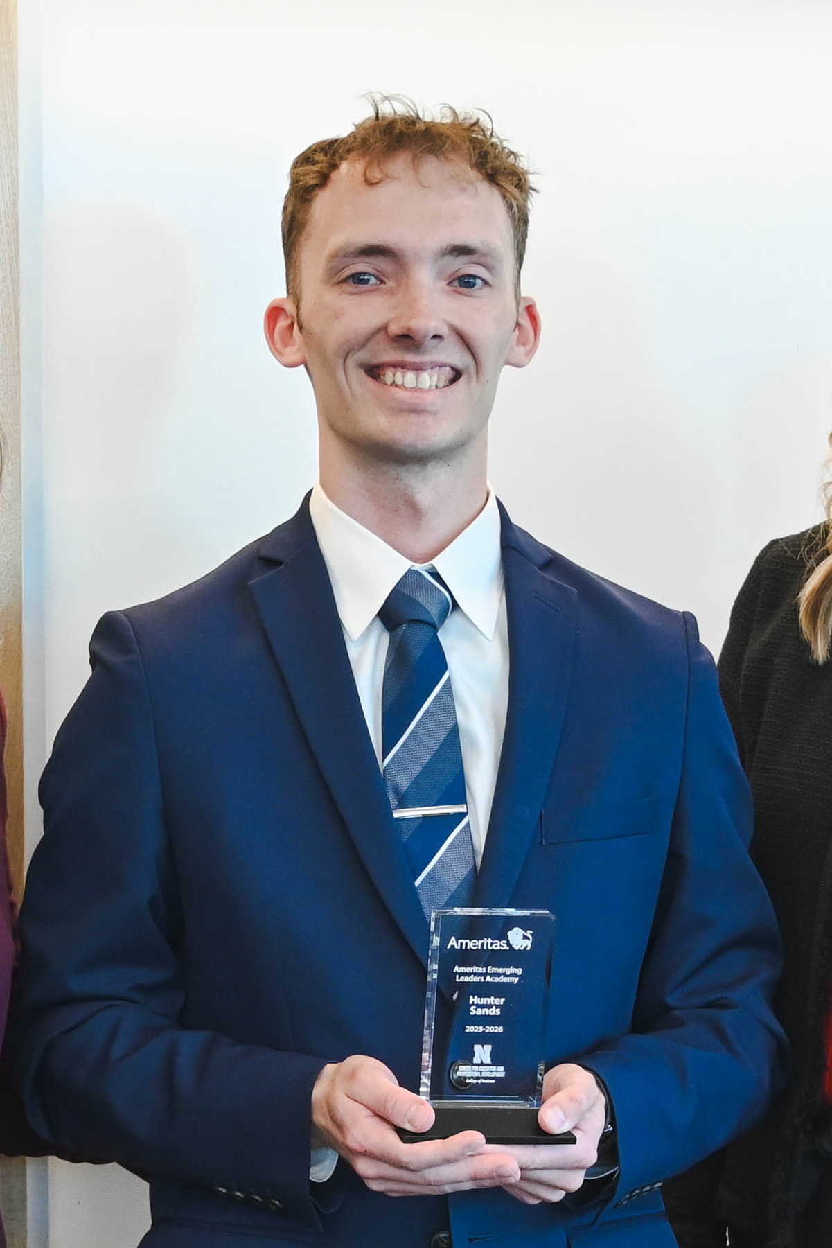 Man in blue suit holding an award, standing in a formal setting with blurred background.