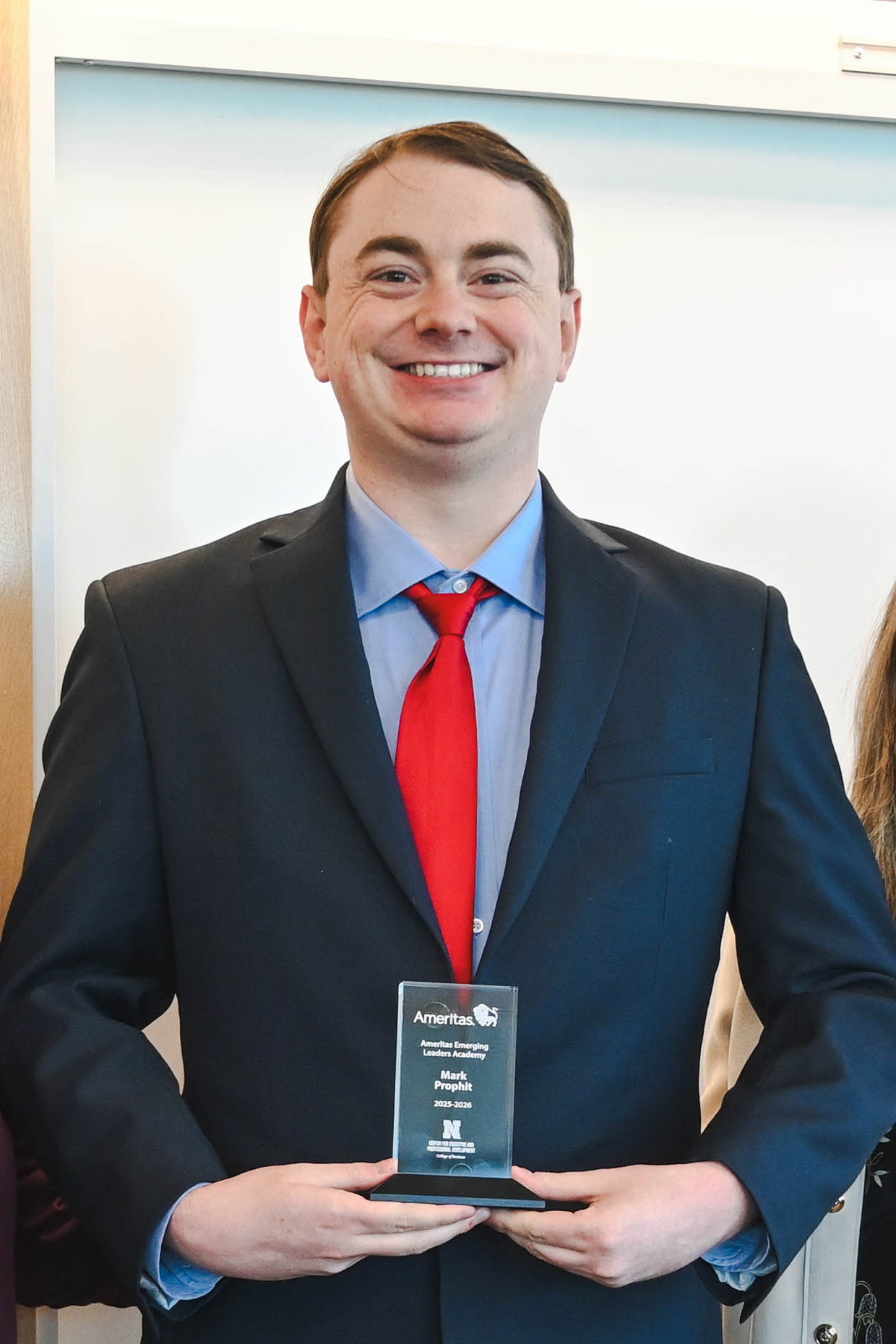 Man in a suit holding a plaque with both hands; white background.