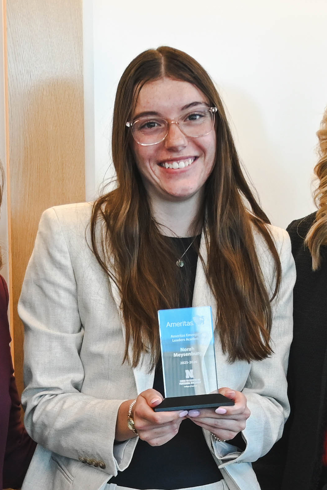 Woman holding an award plaque, dressed in a beige blazer, standing indoors.