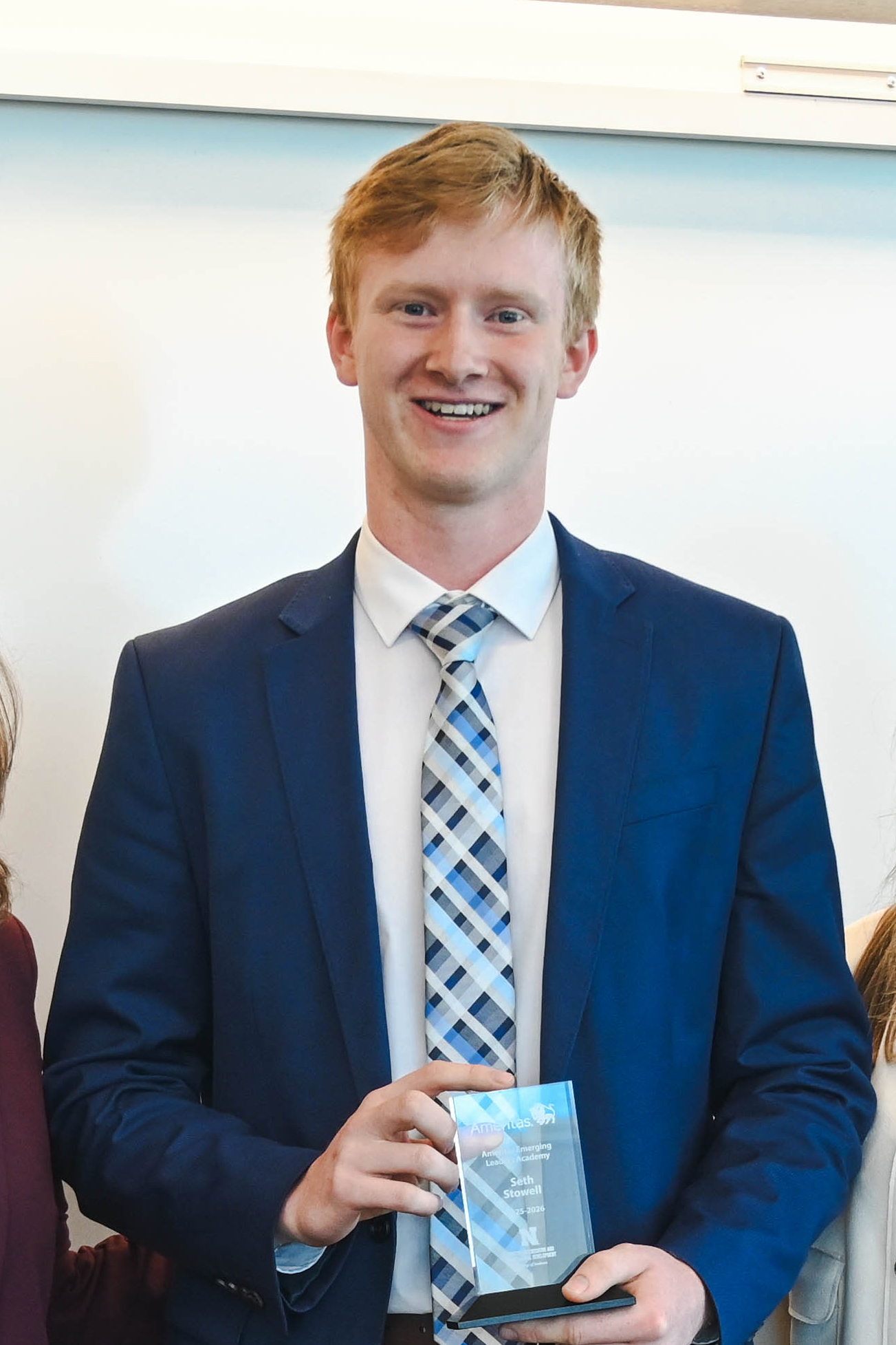 Man in a blue suit holding a glass award, standing indoors.