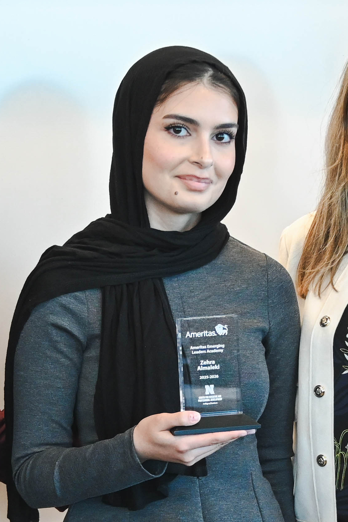 Woman in a black hijab holding a clear award plaque, standing beside another person.