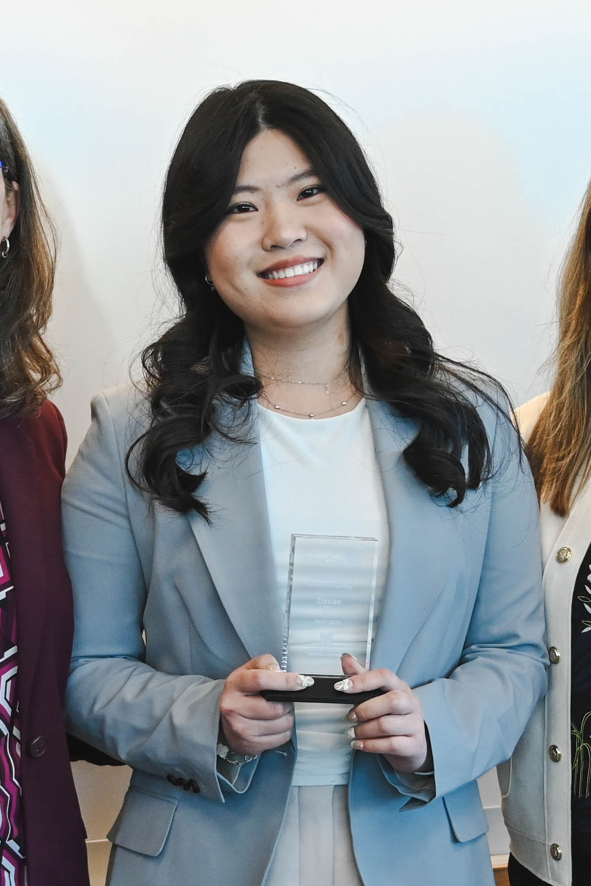 Person in a light blue blazer holding a glass award, flanked by others in professional attire.