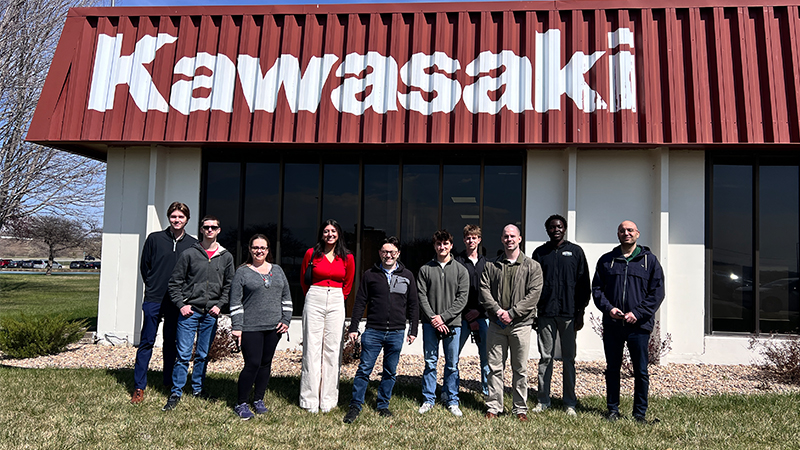 Group of people standing outside a building with a red Kawasaki sign.