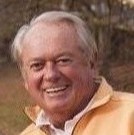 Hal Johnson; Smiling man wearing a yellow sweater in an outdoor setting with blurred foliage.