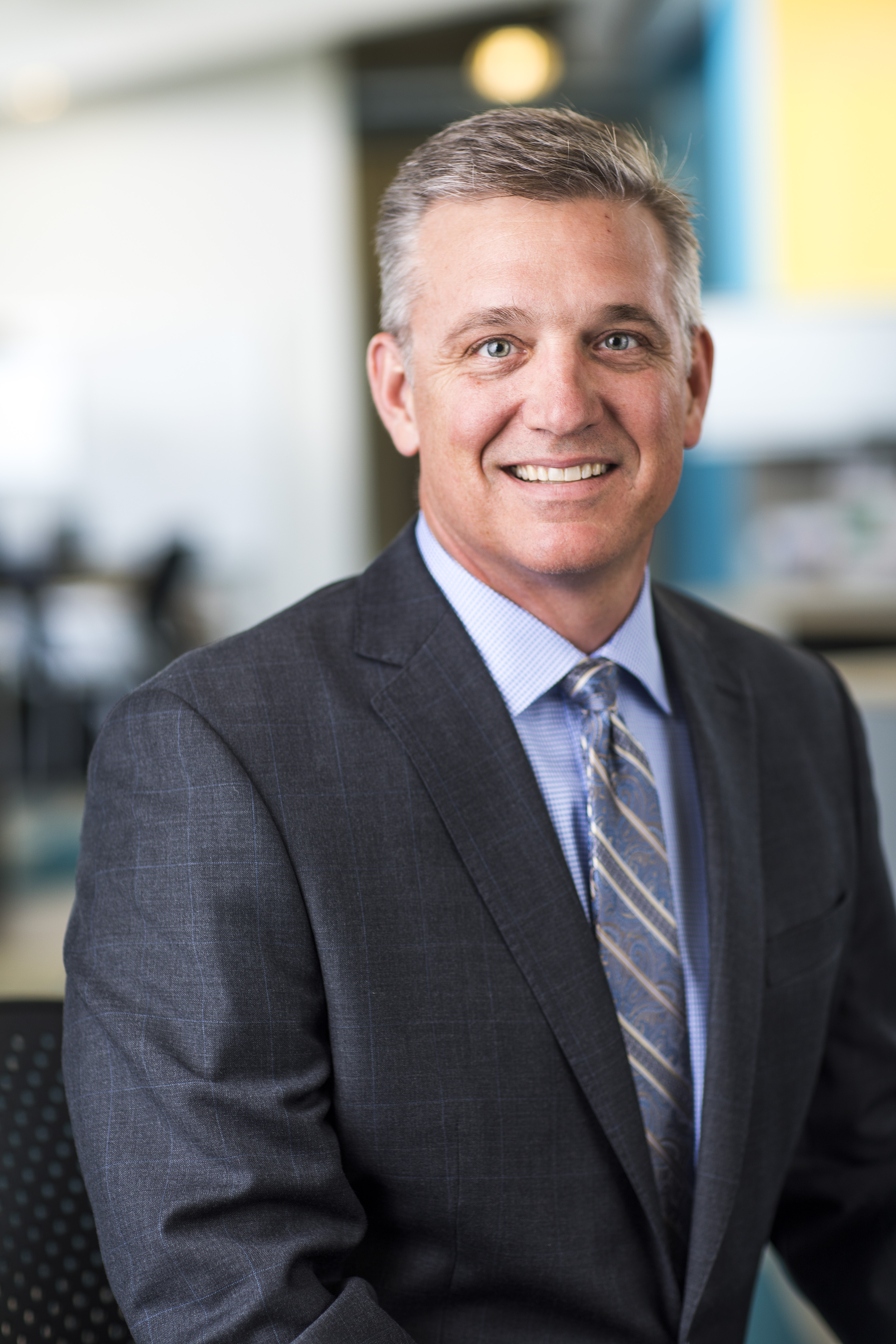 Bill Ellerbee; Smiling man in a gray suit and patterned tie seated in an office setting.