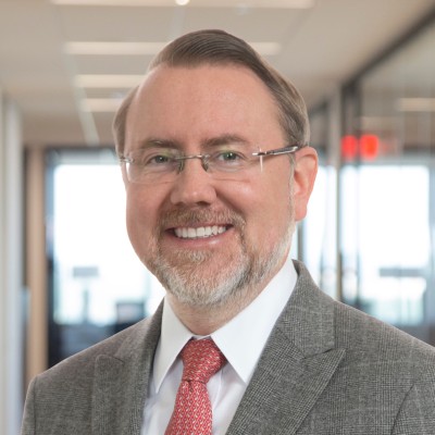Patrick Allen; Smiling man in a suit and tie in an office hallway.