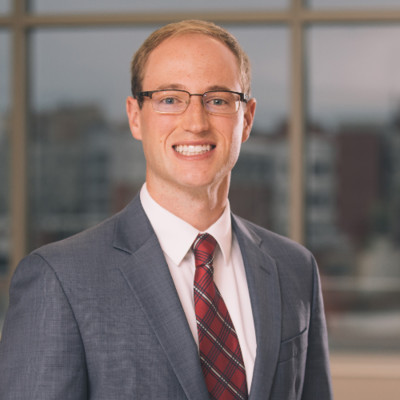 Max Rodenburg; Smiling man in a suit and tie, standing in front of a blurred urban background.