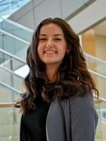 Smiling woman in business attire standing near modern glass staircase.