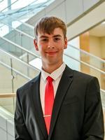 Smiling young man in a suit and red tie near modern staircase indoors.
