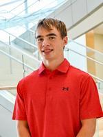Young man in a bright red polo shirt standing in a modern building with glass and stairs.