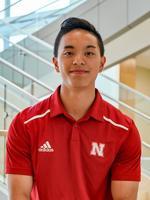 Man wearing red Nebraska polo shirt standing in a modern space with stairs in the background.