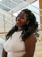 Woman smiling indoors near glass railing and stairs.