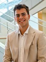 Smiling man in a beige suit near modern glass stairs.