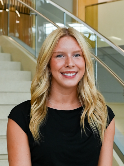 Smiling woman with blonde hair in front of indoor staircase.