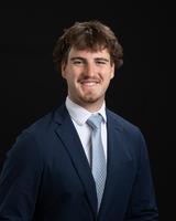 Man in a suit and tie smiling against a black background.
