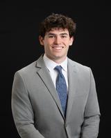 Man in a gray suit and blue tie smiling against a black background.