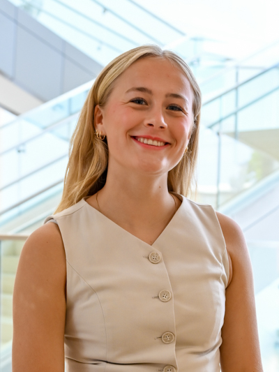 Smiling woman in beige sleeveless top standing in front of glass staircases indoors.