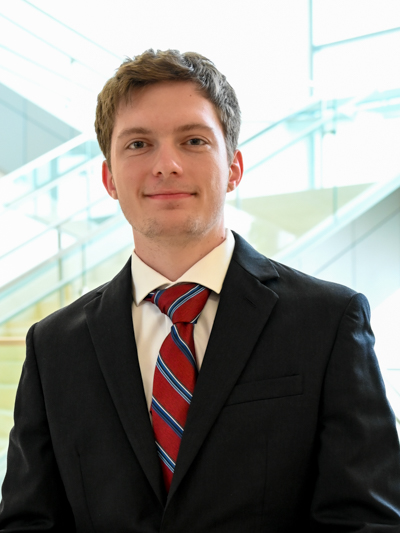 Man wearing a suit and red striped tie, standing in front of a modern glass stairway.