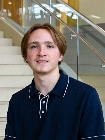 Young man wearing a navy polo shirt, sitting near stairs in a modern building.