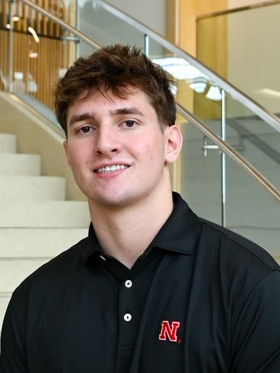 Man in a black shirt with a red "N" logo, standing in front of stairs and glass railing indoors.